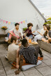 © Maskot - Group of happy multiracial friends having while sitting in balcony during party