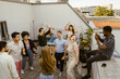 © Maskot - Man photographing group of friends dancing in party in balcony