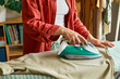 Unrecognizable  middle aged woman ironing washed clothes on ironing board at home. Housewife daily routine. Housekeeping concept.
