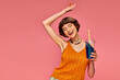 excited young woman with short brunette hair holding refreshing summer drink over head on pink