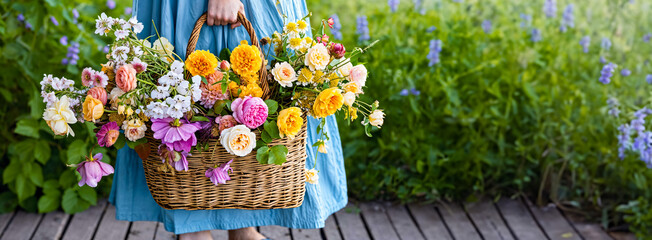 Poster - A woman is holding a wicker basket full of garden flowers. Floral gardening concept