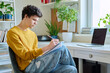 Guy college student sitting at home, looking at laptop screen, making notes in notebook