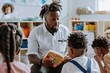 © evgenia_lo - African male teacher reading a book to attentive students.
