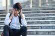 Heartbroken young businessman of Asian beauty talking on the phone holding his head and sitting on stairs in the street