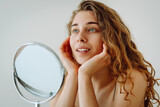 Fototapeta Kuchnia - Young woman with red spot unhappy about acne and skin imperfections, looking at reflection in mirror in bathroom. Facial skin care. Acne problem.