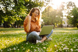 Fototapeta Kuchnia - Young curly woman in the park with laptop on the green grass. Education online. IT. Business, blogging, freelance concept.
