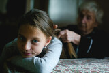 Fototapeta Sawanna - Grandma braiding a little girl's hair.
