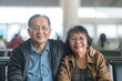 Happy elderly Asian couple sitting at the airport waiting to catch their flight