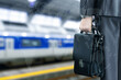 A businessman with a briefcase in his hands at a train station.