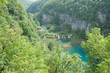 Sheer rock wall and greenery surrounding lake and waterfalls below Croatia