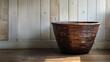   A brown basket rests atop a weathered wooden floor Nearby, a wooden wall casts a long shadow