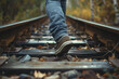 Close-up of a person's foot walking on railroad tracks in autumn.