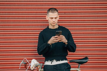 Wall Mural - young man with mobile phone and bicycle on the street in red background