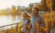 Handsome middle-aged smiling man jogging with beautiful wife by city park along the pond enjoying sunny day together. Sporty active people, healthy lifestyle concept training image.