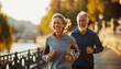 Handsome middle-aged smiling grey haired couple jogging by city park with pond, enjoying sunny evening together. Sporty active people, healthy lifestyle concept training image.