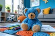 A cute blue teddy bear sits amongst drawing materials on a colorful mat transmitting playfulness and creativity