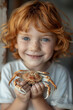 A red-haired child with freckles holding a crab with a gentle smile.