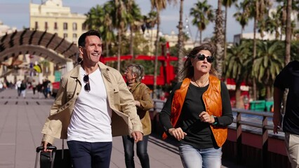 Wall Mural - Group of four middle-aged multiracial tourist people running with their luggage down the street because they are late for their trip destination. Smiling tourism friends travel on vacation in a hurry