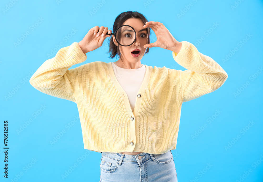 Shocked young woman with magnifier on blue background