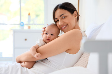 Happy mother with cute little baby lying on bed in room at home