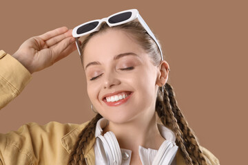 Wall Mural - Beautiful young happy woman with sunglasses and headphones on brown background