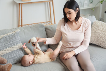 Wall Mural - Young woman with toy and her baby suffering from postnatal depression on sofa at home