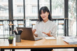 © Satori Studio - A cheerful young businesswoman is engaged in a video call on her laptop in a bright office space.