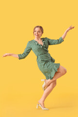 Wall Mural - Beautiful young happy woman dancing on yellow background