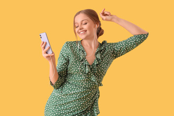 Wall Mural - Beautiful young happy woman in headphones with mobile phone dancing on yellow background