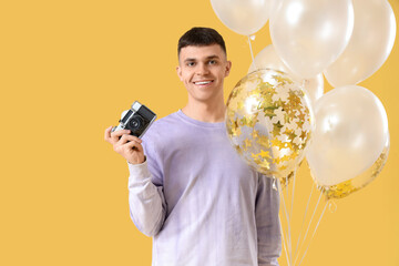 Sticker - Young man with bunch of balloons and photo camera on yellow background