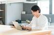 © buritora - ダイニングで朝食中にパソコンでリモートワーク・テレワークする若いアジア人男性