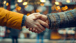 © Nano Photos - Two people in jackets shaking hands, against a blurred background with warm bokeh lights, symbolizing agreement or greeting.