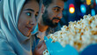 close up shot of casually dressed arabic couple deciding on what flavour of popcorn they want at the blue colored cinema kiosk. we see their face and the popcorn is in the foreground.