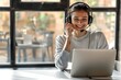 a customer support operator smiling warmly as they speak into their headset looking at the laptop