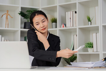 Wall Mural - Business woman looking busy while talking on mobile and searching through document on messy table in an office