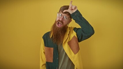 Wall Mural - Cheeky redhead guy dons glasses and shirt, pulling the classic 'loser' gesture on forehead, laughing as he mocks and insults folks. solo show over a punchy yellow backdrop.