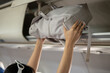 © bongkarn - A close-up image of a female passenger is putting her bag in an overhead bin, traveling by plane.