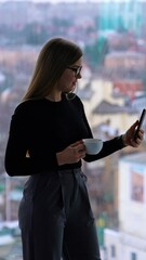 Sticker - Young caucasian woman wearing glasses while talking by phone and drinking coffee. Coworking concept. Vertical video