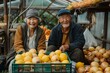 A man and a woman are seated beside a crate of fresh fruit at a greengrocers market. They smile as they admire the natural foods and whole food produce on display