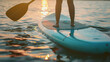 Woman standing on a board doing paddle boarding activity at sunset