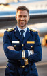 Portrait of a smiling airline pilot with arms crossed in front of an airliner welcoming passengers on board