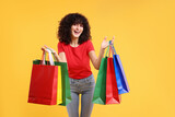 Fototapeta Mapy - Happy young woman with shopping bags on yellow background