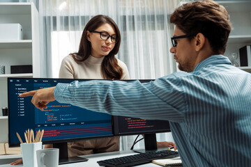 woman colleague standing opposite to man programmer working on desk to discuss coding website softwa