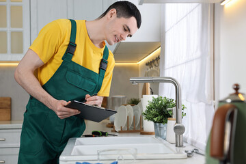 Canvas Print - Smiling plumber with clipboard examining faucet in kitchen