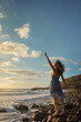 A beautiful young woman on a rocky beach, with her arms outstretched as she embraces the wind and breathes in the fresh, salty air. Peace and tranquility concept.