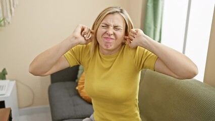 Poster - Annoyed young blonde woman wearing t-shirt covers ears with fingers, stressed by loud music noise at home – deaf expression