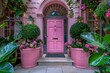 A pink door with a gold knob sits in front of a house with pink flowers in pots