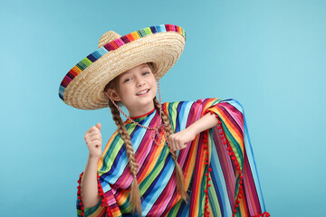 Wall Mural - Cute girl in Mexican sombrero hat and poncho dancing on light blue background