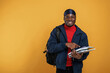 Student with books, backpack and notepad. Handsome black man is in the studio against yellow background