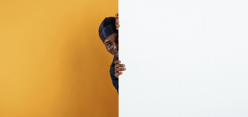 Wall Mural - White copy space, smiling and hiding behind it. Handsome black man is in the studio against yellow background